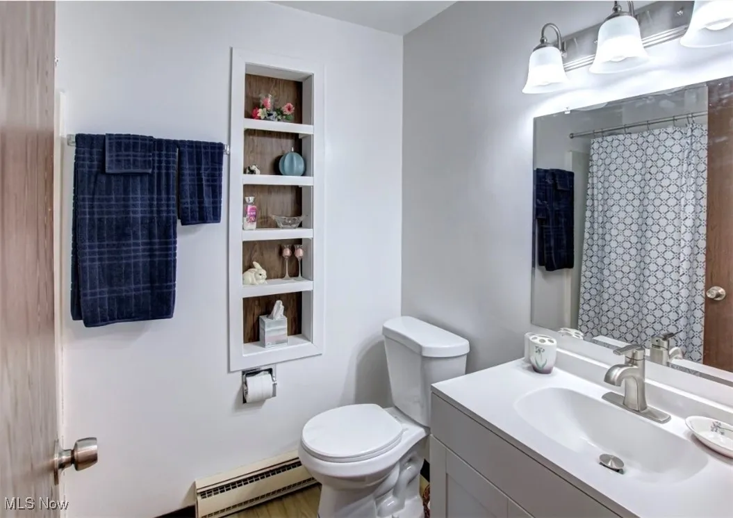Full bath featuring vanity, baseboard heating, curtained shower, and built in shelves