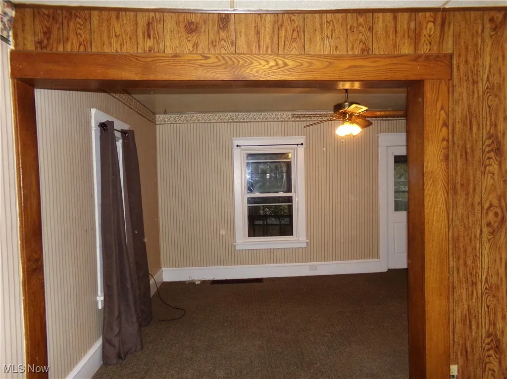 Empty room with dark colored carpet, wood walls, and a ceiling fan