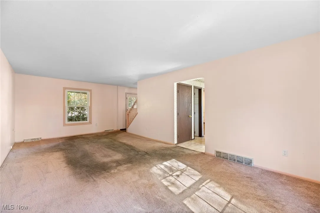 Carpeted spare room featuring baseboards and stairway