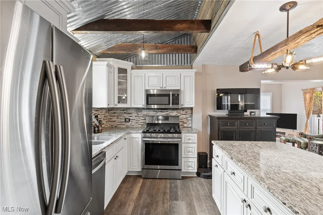 Kitchen featuring white cabinets, stainless steel appliances, beamed ceiling, backsplash, and light stone counters