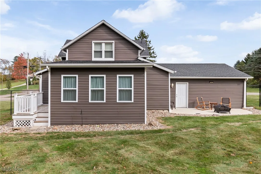 Back of house with a fire pit, roof with shingles, a deck, and a patio