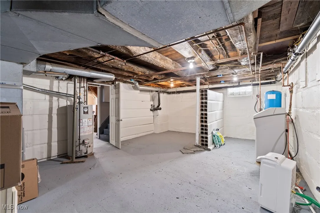 Unfinished basement featuring a water softener, water heater, and a water pressure tank