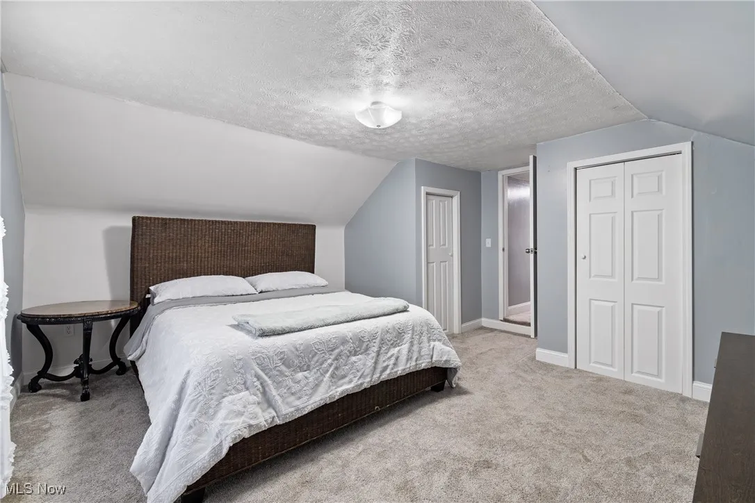 Bedroom featuring a textured ceiling, light carpet, lofted ceiling, and a closet