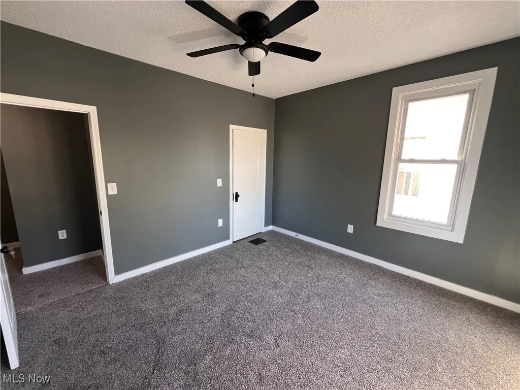Empty room with a textured ceiling, dark colored carpet, and a ceiling fan