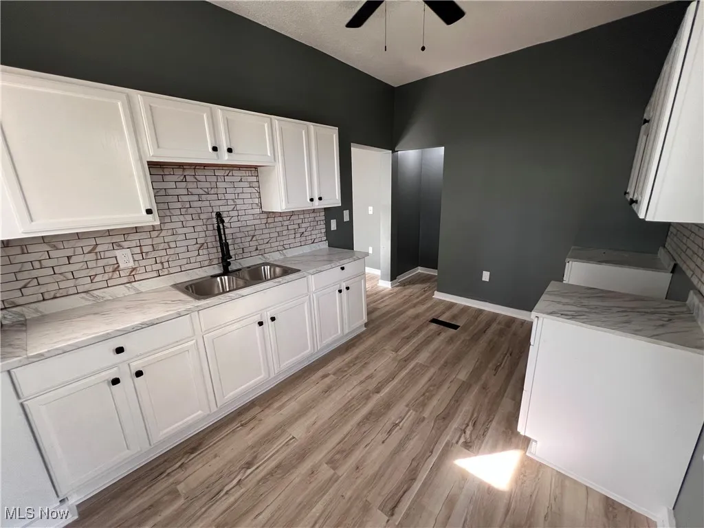 Kitchen with white cabinets, backsplash, light wood-style floors, a ceiling fan, and light stone countertops