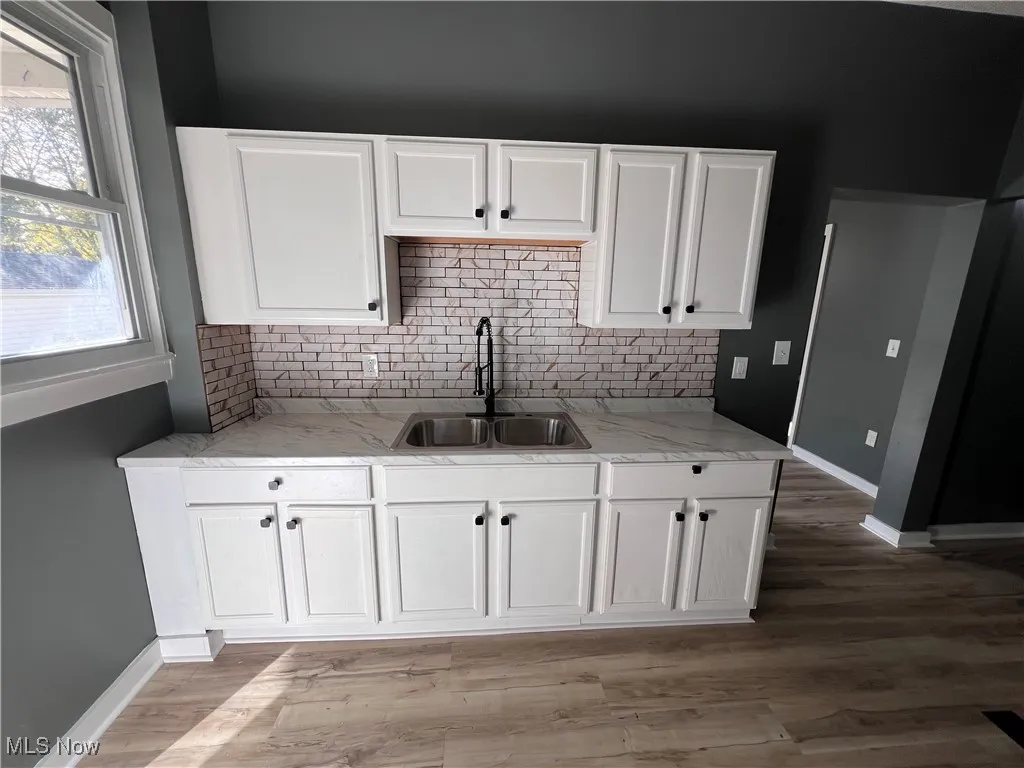 Kitchen with white cabinetry, tasteful backsplash, light wood-style flooring, and light countertops