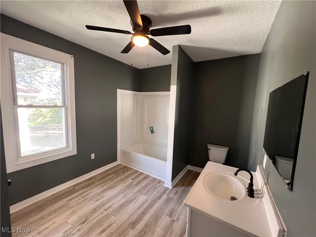 Full bath featuring vanity, light wood-type flooring, a textured ceiling,  shower combination, and ceiling fan