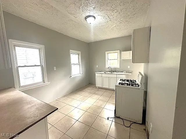 Kitchen with white cabinetry, white gas stove, a textured ceiling, light tile patterned floors, and light countertops