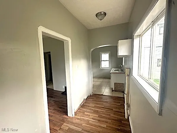 Hallway featuring arched walkways, dark wood finished floors, and a textured ceiling