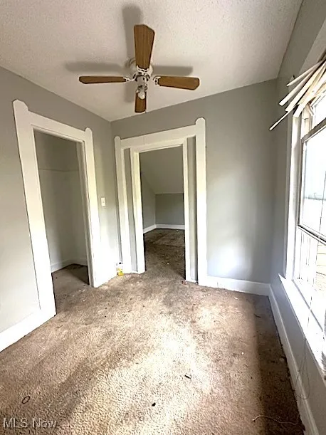 Unfurnished bedroom with a textured ceiling, a ceiling fan, and a spacious closet