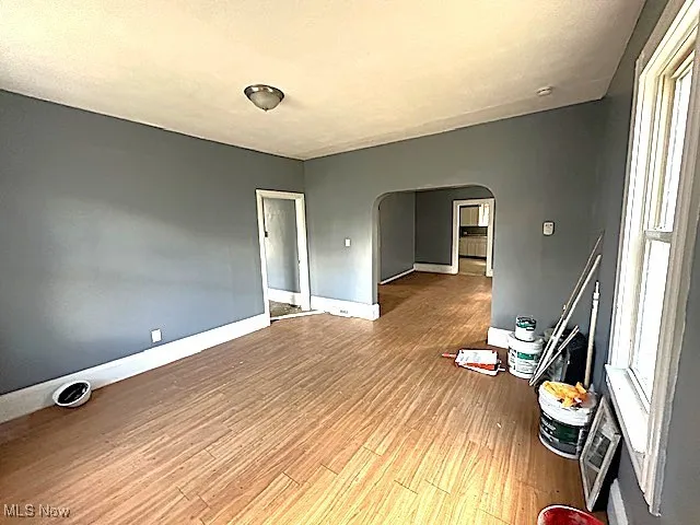 Spare room with arched walkways, light wood-style floors, and plenty of natural light