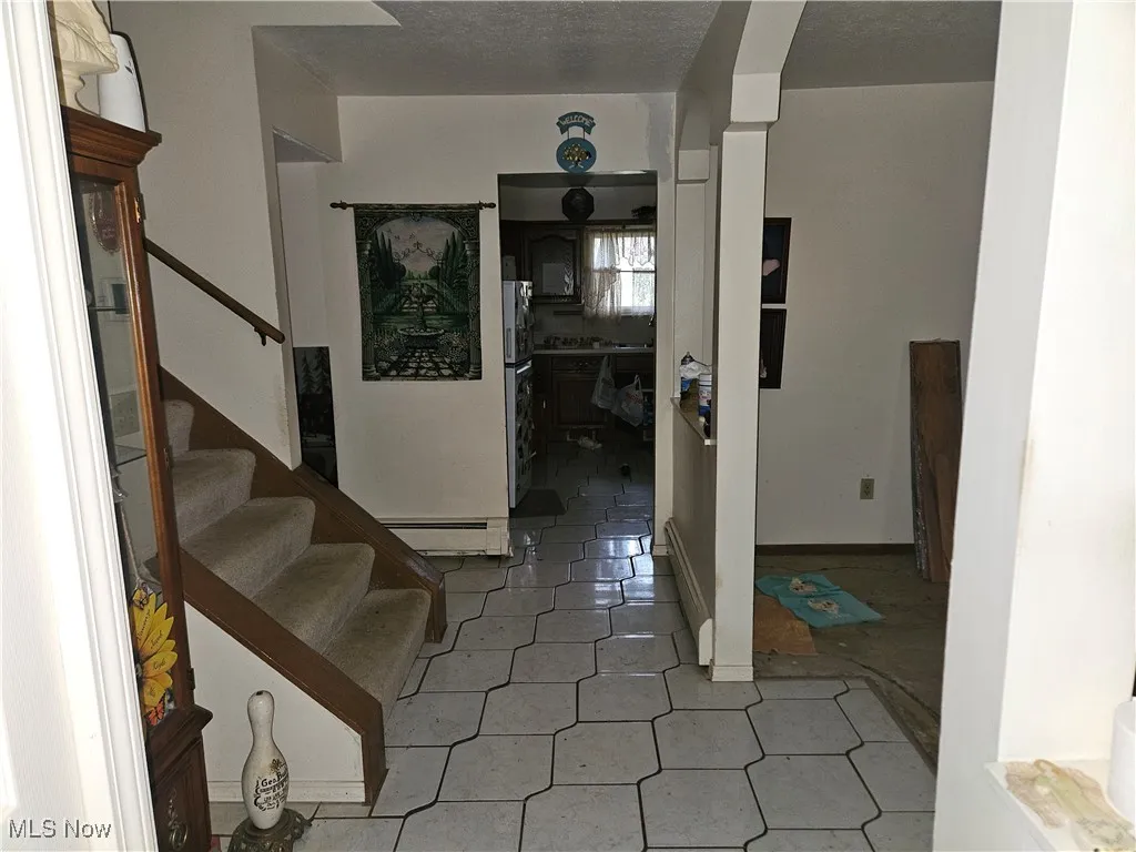 Foyer featuring stairway, a baseboard radiator, a textured ceiling, arched walkways, and light tile patterned flooring