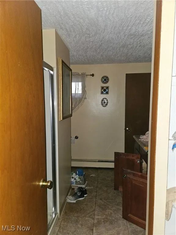 Full bathroom featuring a stall shower, a baseboard heating unit, a textured ceiling, and dark tile patterned flooring