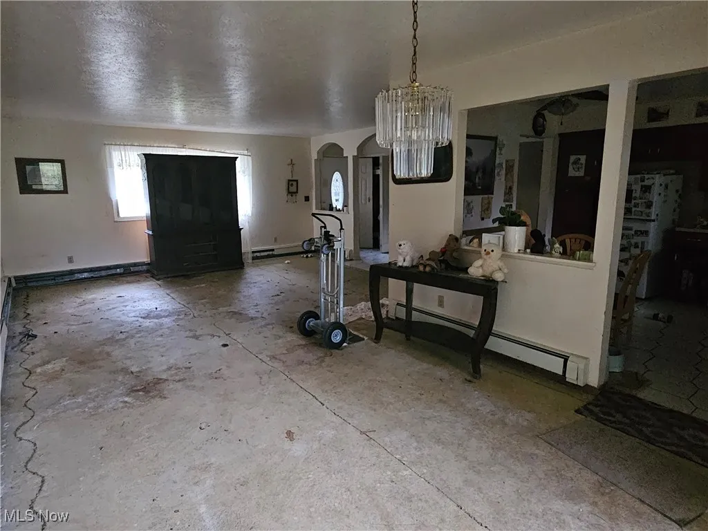 Foyer entrance featuring a baseboard radiator, arched walkways, a textured ceiling, unfinished concrete floors, and a chandelier