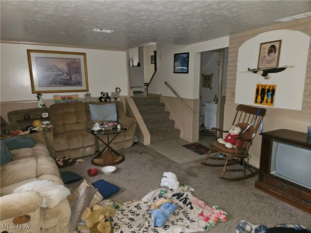 Carpeted living room featuring a textured ceiling, a wainscoted wall, and stairs