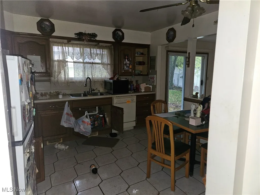 Kitchen featuring light countertops, white appliances, a ceiling fan, dark brown cabinets, and light tile patterned floors
