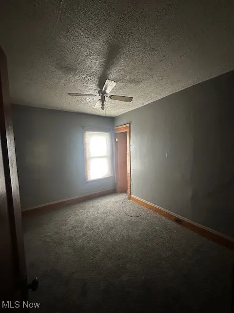 Carpeted empty room with a textured ceiling and ceiling fan