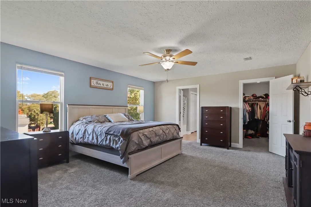 Carpeted bedroom featuring a spacious closet, a textured ceiling, and a ceiling fan