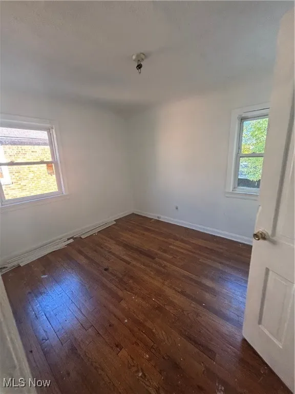 Spare room featuring dark wood-type flooring and baseboards