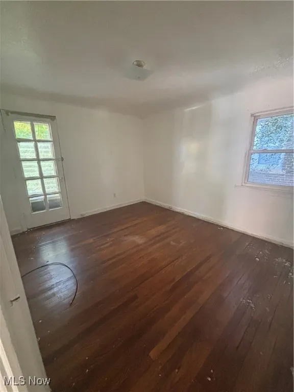 Spare room featuring dark wood-style flooring and baseboards
