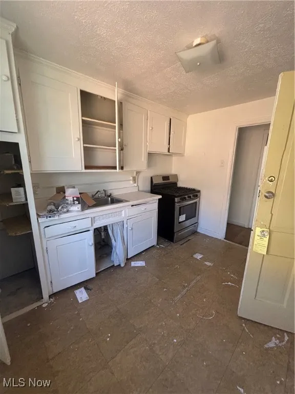 Kitchen with white cabinetry, range, light countertops, a textured ceiling, and open shelves