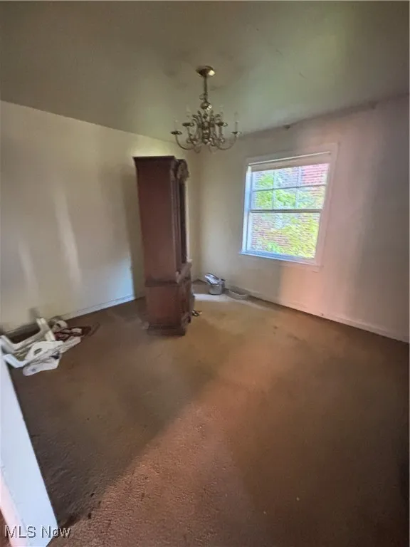 Unfurnished dining area featuring a chandelier and carpet flooring