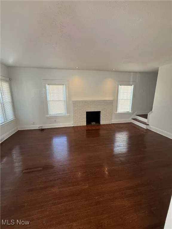 Unfurnished living room featuring a fireplace, dark wood-style floors, and a textured ceiling