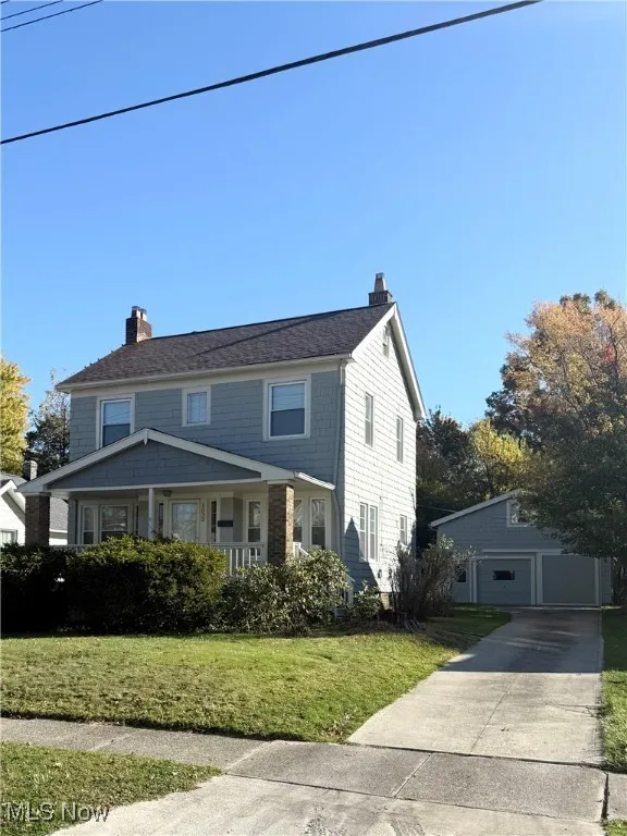 View of front of property featuring a chimney, covered porch, an outbuilding, a front yard, and a garage