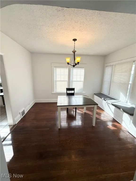 Unfurnished dining area featuring a textured ceiling, dark wood finished floors, and a chandelier