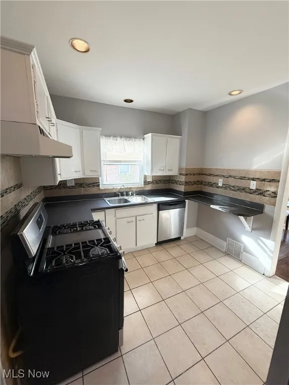 Kitchen featuring gas stove, white cabinets, light tile patterned floors, dishwasher, and under cabinet range hood