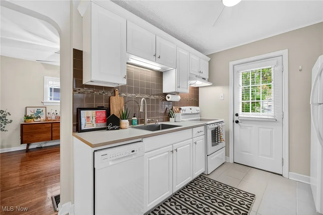 Kitchen featuring white cabinets, white appliances, light countertops, and backsplash