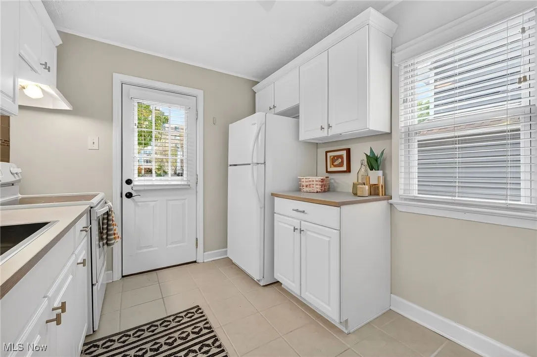 Kitchen with white cabinets, white appliances, light countertops, light tile patterned floors, and ornamental molding