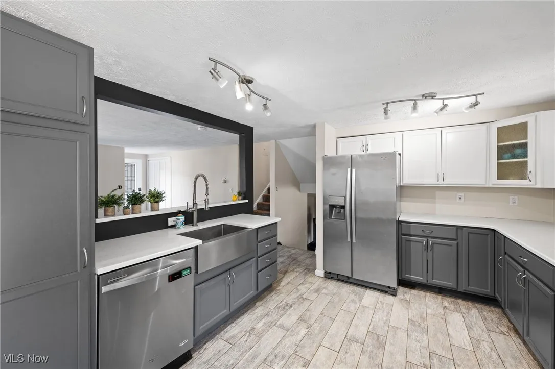 Kitchen with gray cabinetry, stainless steel appliances, a textured ceiling, wood tiled floors, and glass insert cabinets