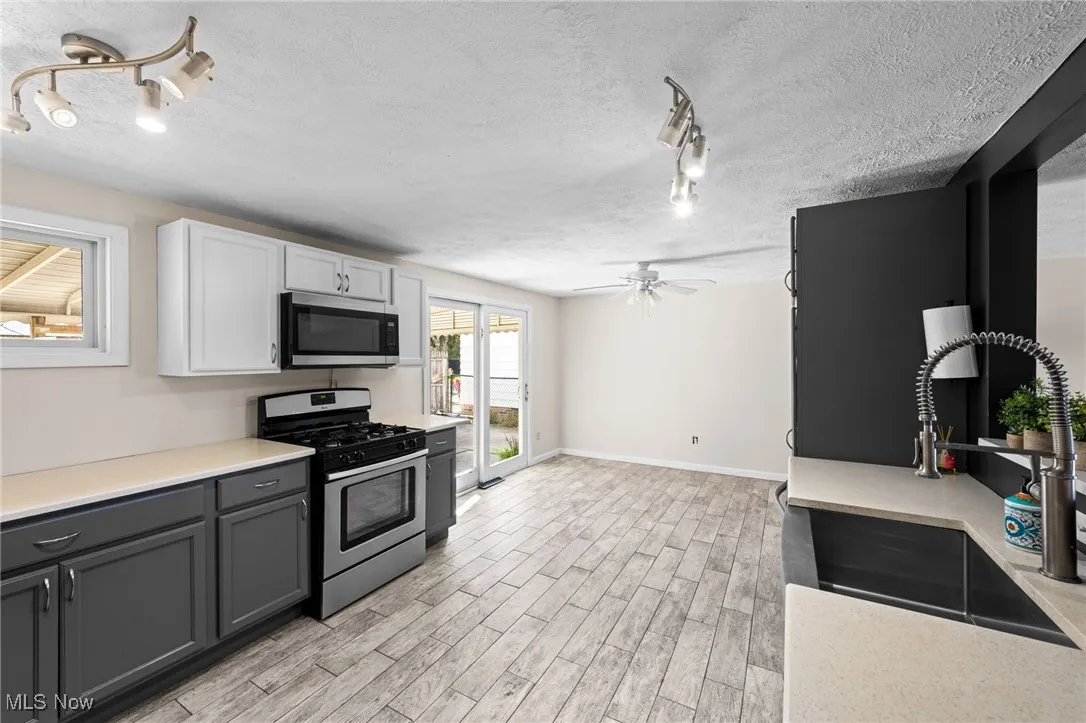 Kitchen featuring rail lighting, appliances with stainless steel finishes, a textured ceiling, light wood-style flooring, and white cabinetry