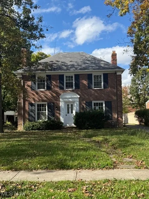 Colonial house featuring a chimney, a front lawn, and brick siding