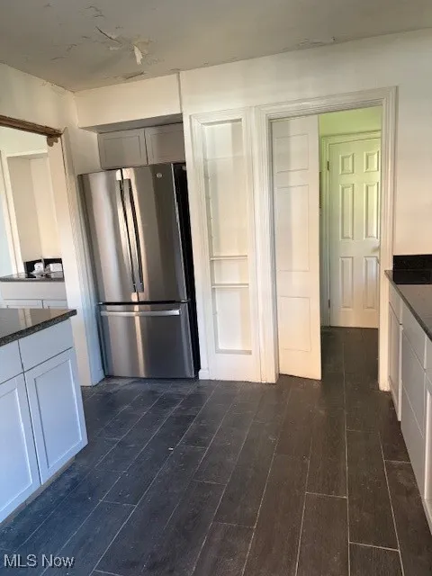 Kitchen with freestanding refrigerator, dark stone counters, dark wood-style floors, and white cabinets