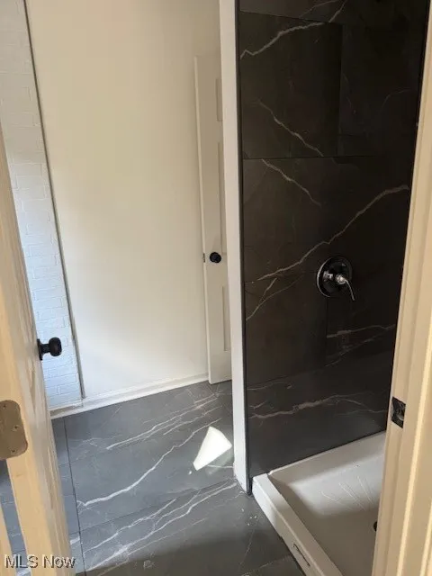 Full bath with a marble finish shower and marble finish flooring