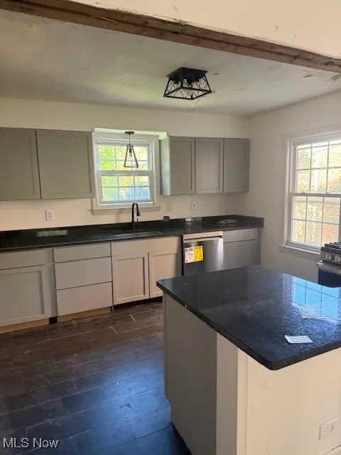 Kitchen featuring dark wood finished floors, gray cabinetry, dishwashing machine, and healthy amount of natural light