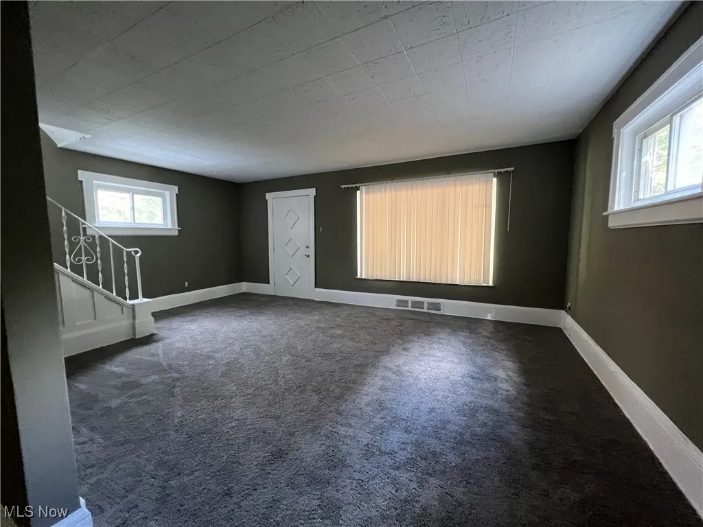 Unfurnished room featuring stairs, dark carpet, and plenty of natural light