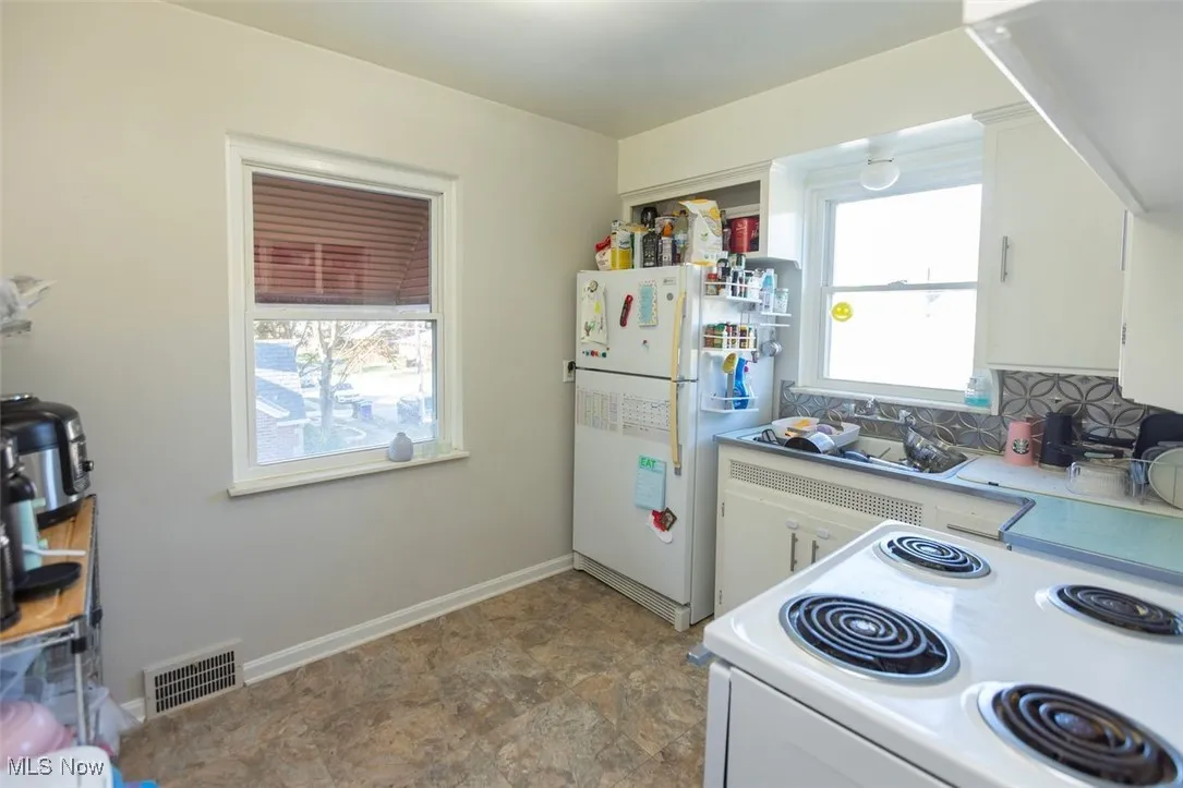Up unit Kitchen featuring white appliances, tasteful backsplash, white cabinets, light countertops, and stone finish floors