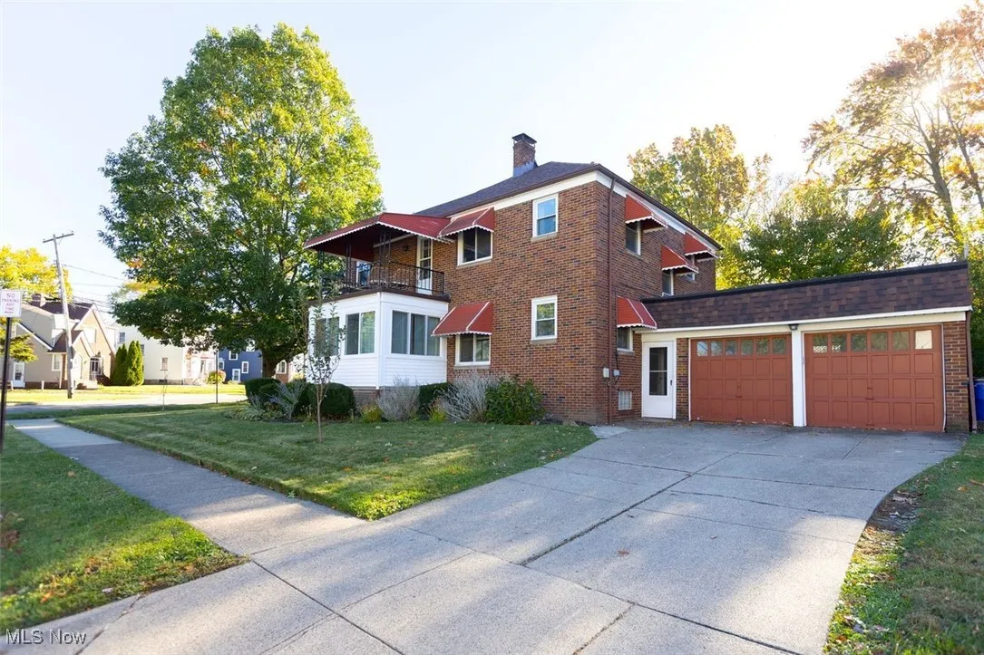 View of the side of the property exterior with a chimney, a balcony, concrete driveway, an attached garage, and brick siding