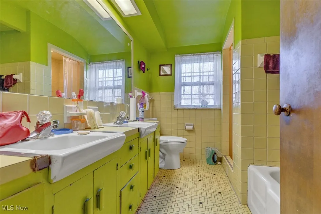 Full bath with tile walls, double vanity, plenty of natural light, a tub - upstairs