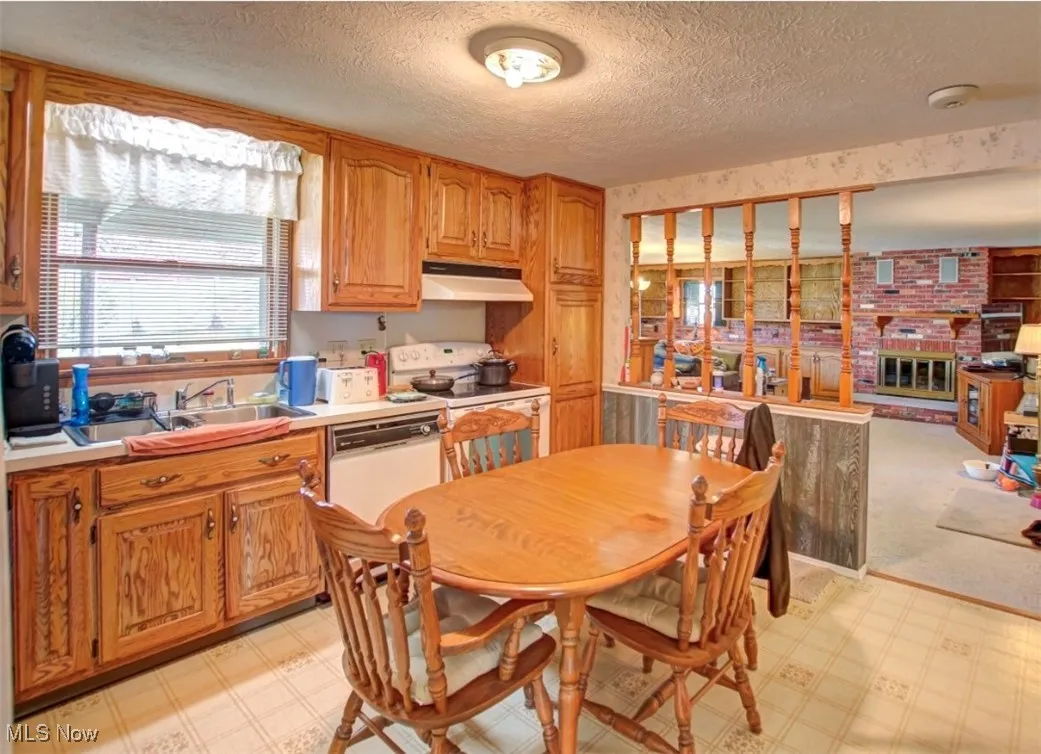 Kitchen with light countertops, white appliances, light floors, a textured ceiling, and under cabinet range hood