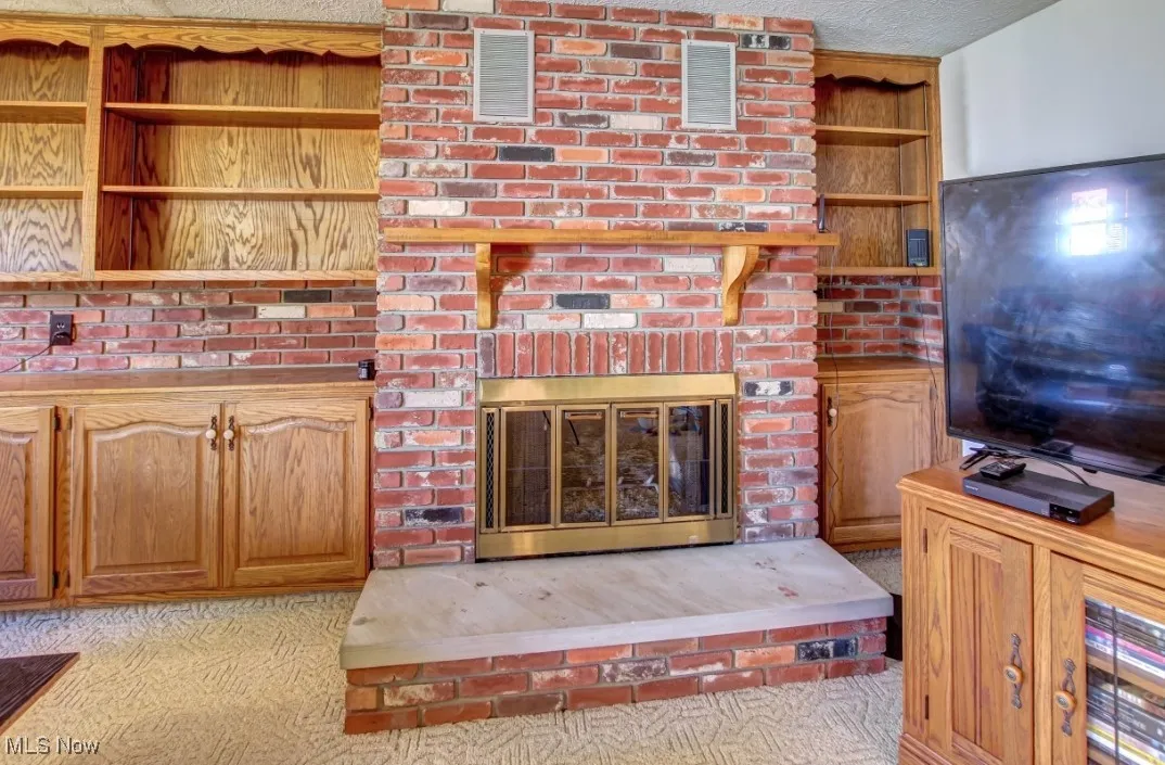 Living area featuring light colored carpet, a textured ceiling, and a brick fireplace