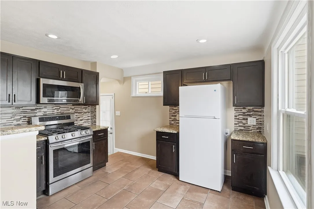 Kitchen with stainless steel appliances, tasteful backsplash, dark brown cabinets, recessed lighting, and light stone counters