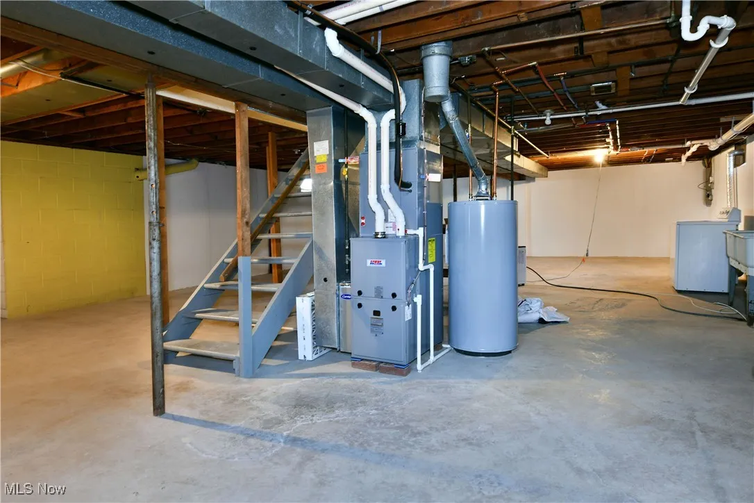Unfinished basement with stairway, water heater, washer / dryer, heating unit, and concrete block wall