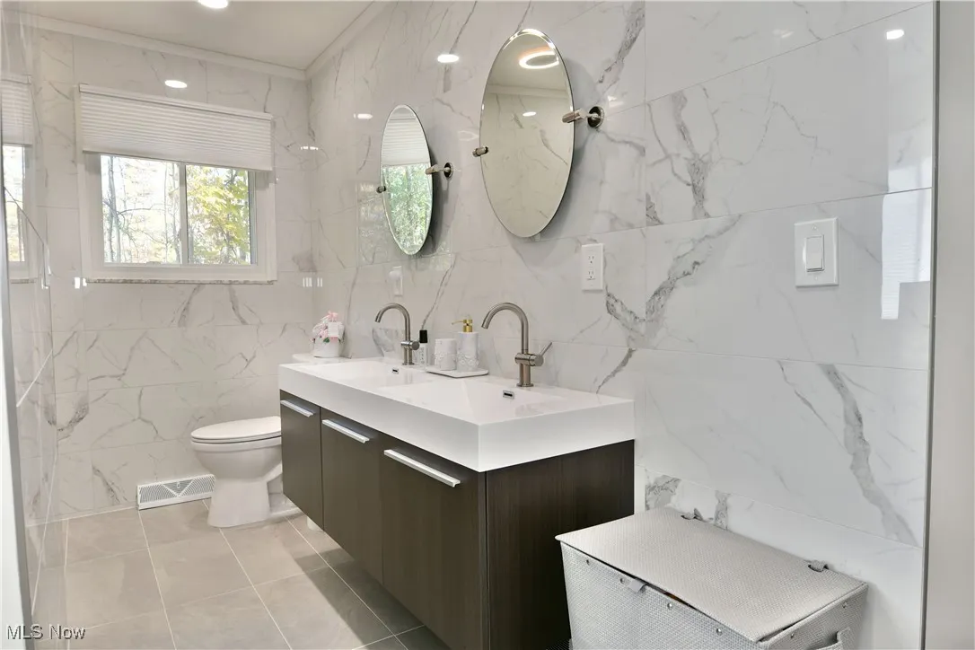 Full bathroom with tile walls, double vanity, light tile patterned floors, crown molding, and recessed lighting