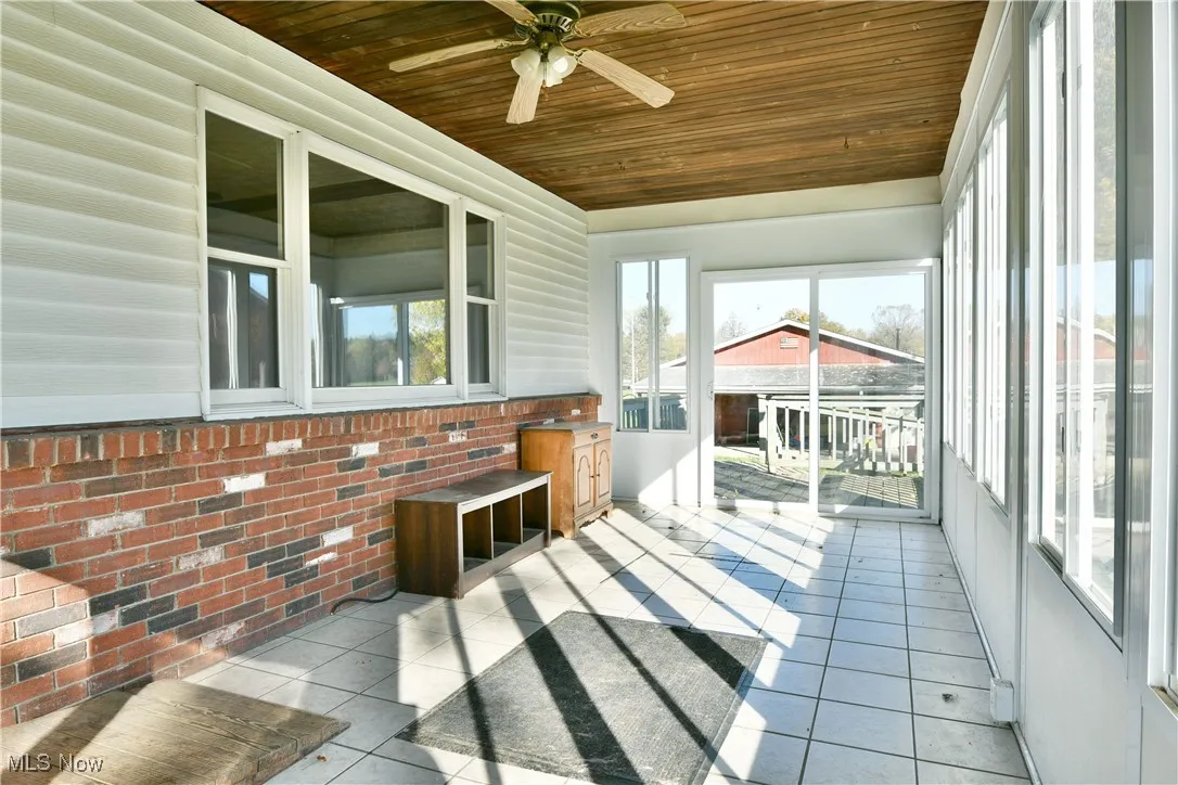 Unfurnished sunroom featuring wood ceiling, plenty of natural light, tile patterned flooring, brick wall, and ceiling fan