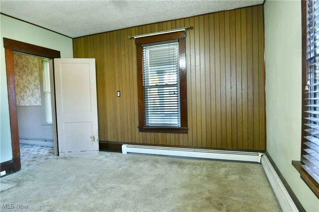 Carpeted empty room featuring wooden walls, baseboard heating, a textured ceiling, and a baseboard radiator