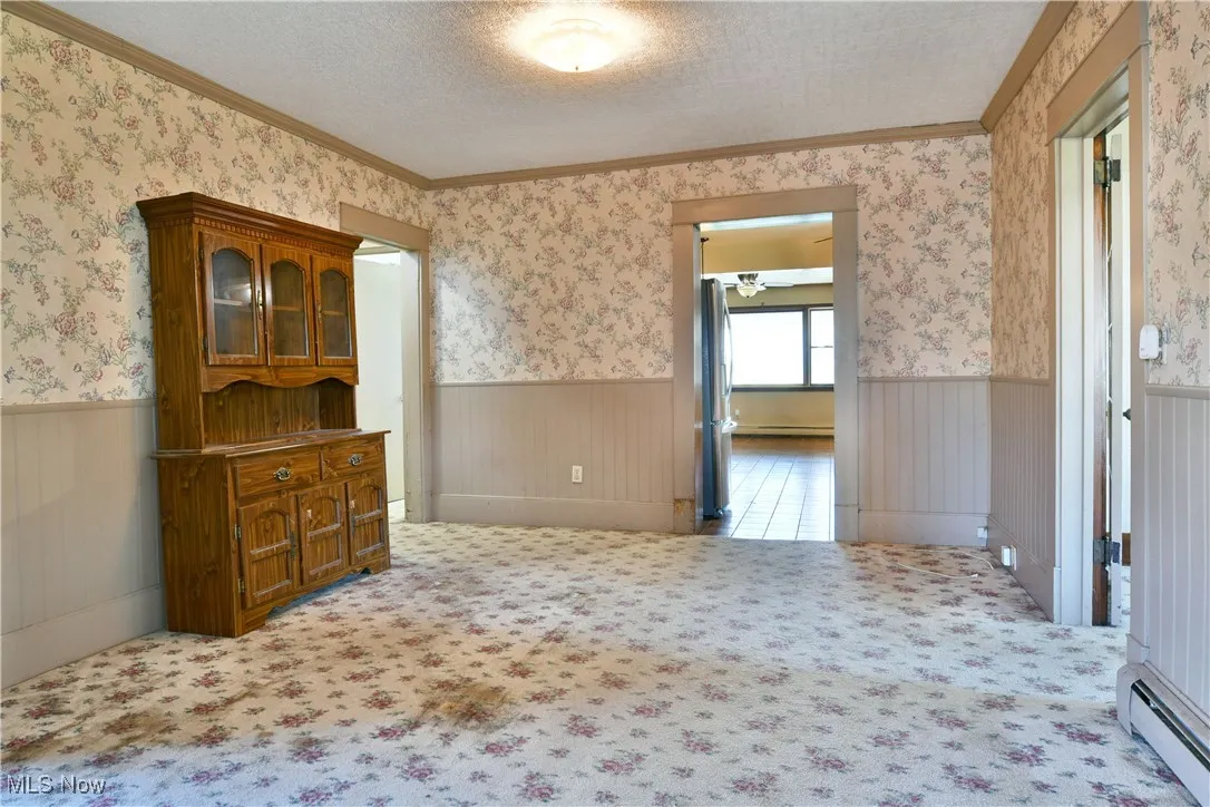 Spare room featuring ornamental molding, light colored carpet, a baseboard radiator, a textured ceiling, and wallpapered walls